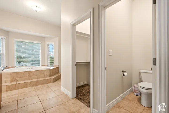 Soaking tub featuring a raised tile surround, built-in storage closet, and ceramic tile flooring