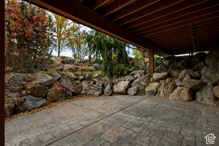 Covered patio featuring stamped concrete flooring, exposed wooden support beams, and a natural rock retaining wall