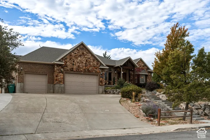 Exterior facade featuring masonry stone and brick cladding, a multi-car garage, pitched rooflines, and tiered concrete landscaping steps with rustic timber fencing