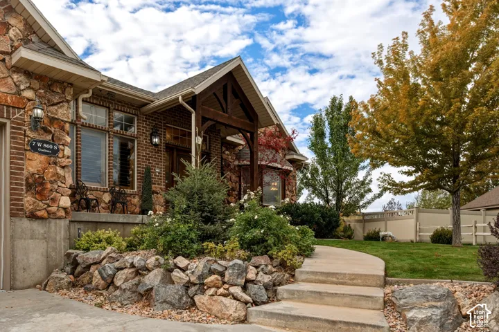 Exterior facade featuring brick and natural stone masonry, a covered porch with timber framing, concrete steps, and landscaped rock gardens