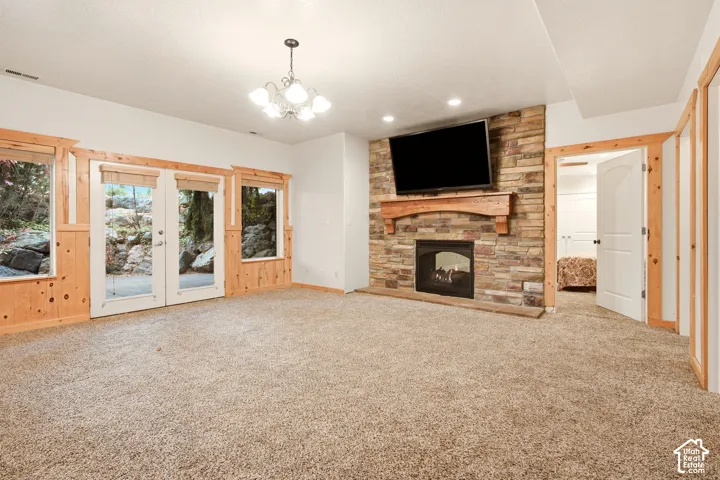 Living area featuring a floor-to-ceiling stone fireplace with a natural wood mantel, wood-trimmed French doors, knotty pine wall paneling, and a multi-arm chandelier