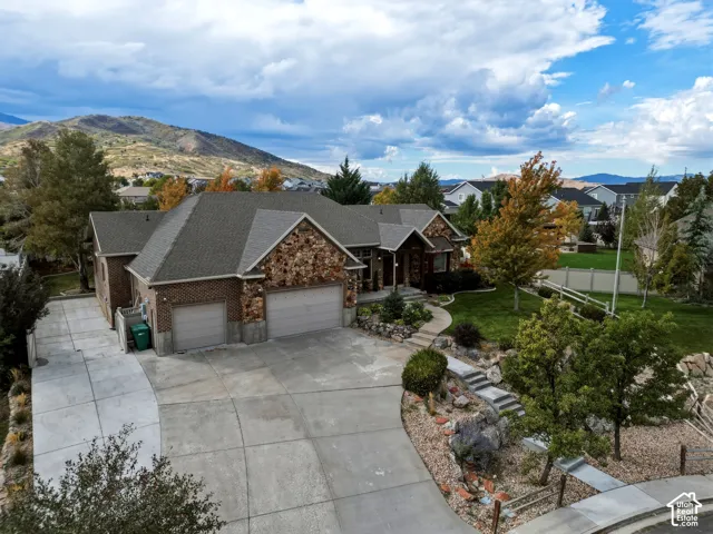 Multi-level residential exterior featuring a brick and stone facade, attached three-car garage, concrete driveway, and professional landscaping with rock gardens