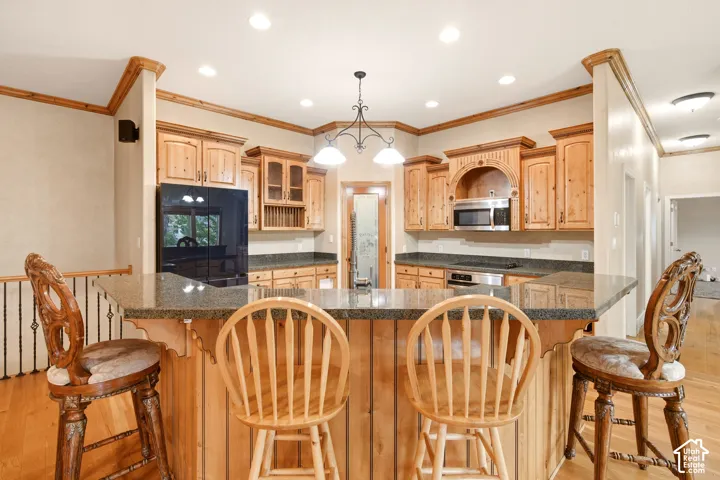 Kitchen featuring wood cabinetry, stone countertops, a raised breakfast bar, recessed lighting, and stainless steel built-in appliances