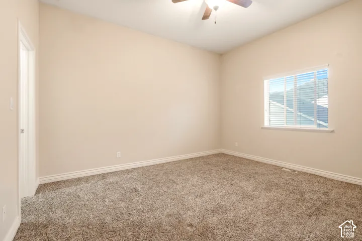 Neutral interior featuring carpeted flooring, a ceiling fan with integrated lighting, and a single-pane window with horizontal blinds