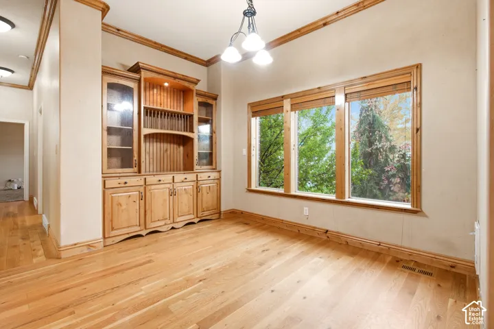Room featuring wood-finish flooring, built-in cabinetry with glass-front shelving, multi-pane windows with wood trim, and a three-light chandelier