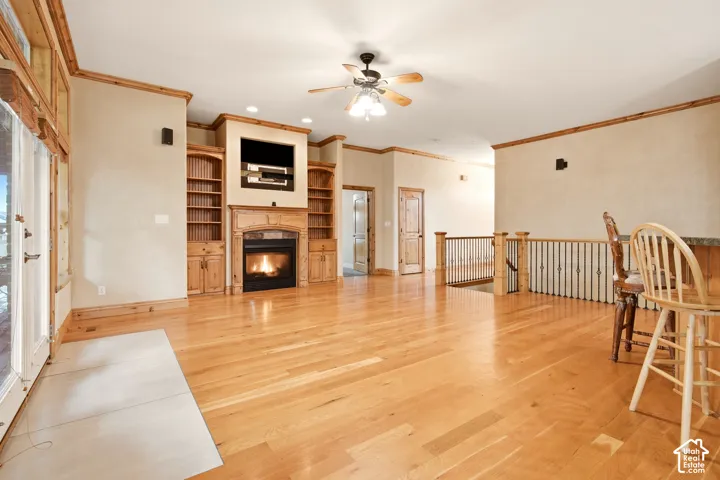 Open living area featuring wood-finish flooring, built-in wooden cabinetry, a fireplace with a stone-surround mantel, and a metal-spindle stair railing