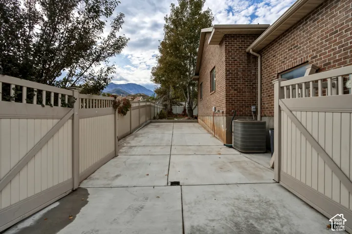 Concrete side yard featuring a brick exterior facade, dual white vinyl privacy gates, and mountain scenery