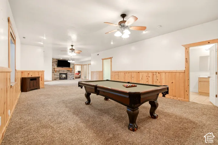 Large interior space featuring natural wood wainscoting, stone-surround fireplace with timber mantel, carpeted flooring, and dual ceiling fans