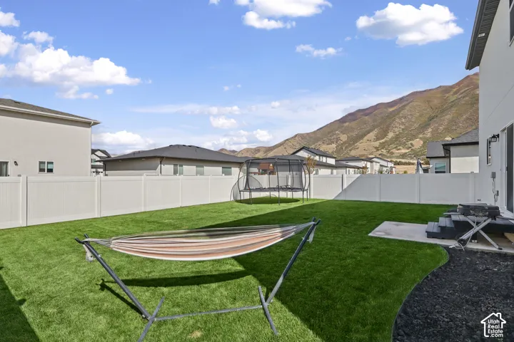 Fenced backyard featuring a manicured lawn, concrete patio, and mountain scenery