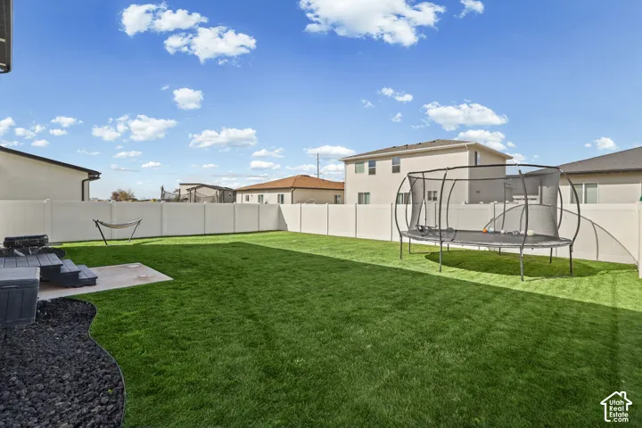 Rear yard featuring a grass lawn, white vinyl fencing, a concrete patio, and a decorative black stone border