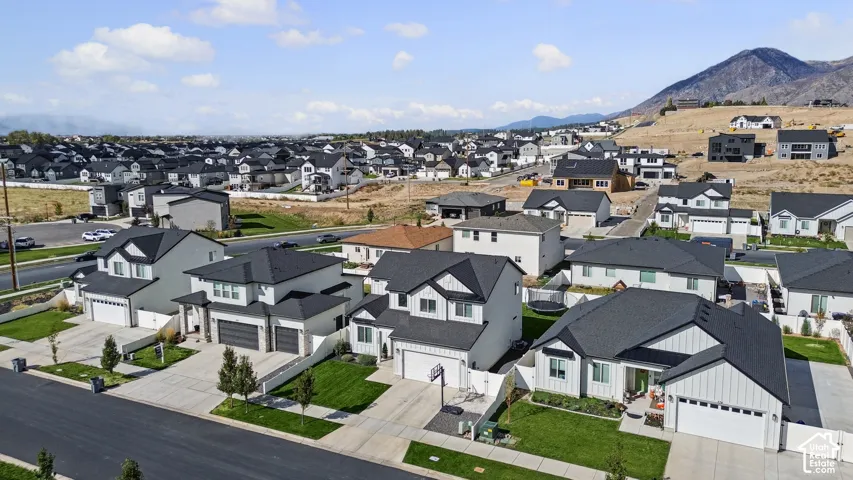 Aerial perspective of a suburban neighborhood featuring residential homes with multi-gabled rooflines, attached garages, manicured lawn areas, and mountain scenery