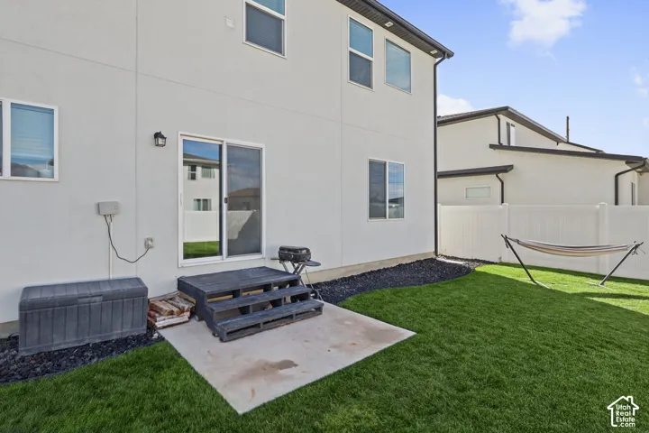 Rear exterior featuring stucco siding, a concrete patio, wood-finish stairs, a fully fenced yard, and black rock landscaping accents