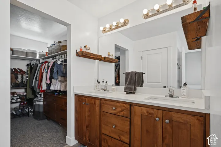 Double vanity featuring stone countertops, integrated dual sinks, wood cabinetry, and wall-mounted shelving