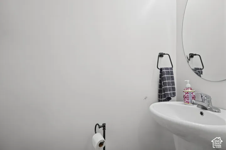 Wall-mounted oval mirror, pedestal sink with chrome faucet, and matte black finish hardware including a towel ring and toilet paper holder