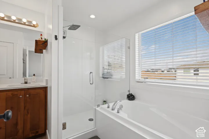Bathroom featuring a wood-finish vanity with a rectangular sink, a glass-enclosed shower with a rainfall showerhead, and a drop-in soaking tub with a deck-mounted faucet