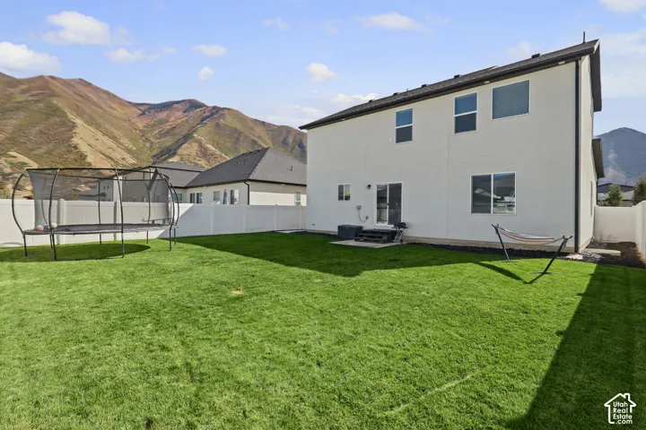 Rear exterior featuring a smooth stucco finish, a fenced-in lawn, concrete patio, and prominent mountain backdrop