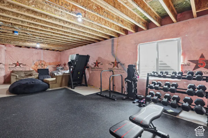 Unfinished lower level featuring exposed wood-beam ceiling joists, pink insulation-wrapped perimeter walls, and rubberized flooring