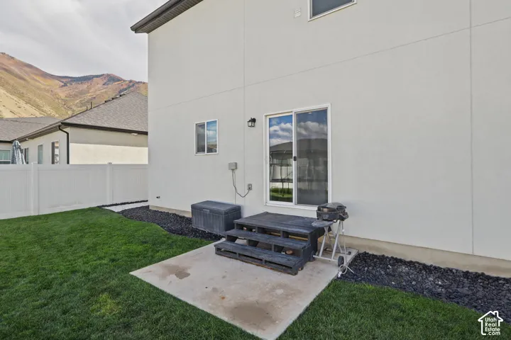 Stucco exterior featuring sliding glass doors, concrete patio, white vinyl fencing, and mountain backdrop