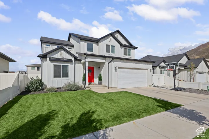 Two-story residence featuring a vertical siding exterior, attached two-car garage, manicured lawn, concrete driveway, and mountain backdrop