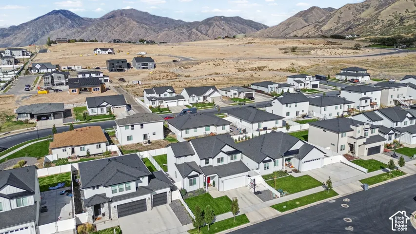 Aerial perspective of residential neighborhood featuring multi-story homes with pitched roofs, integrated multi-car garages, concrete driveways, and mountain backdrop