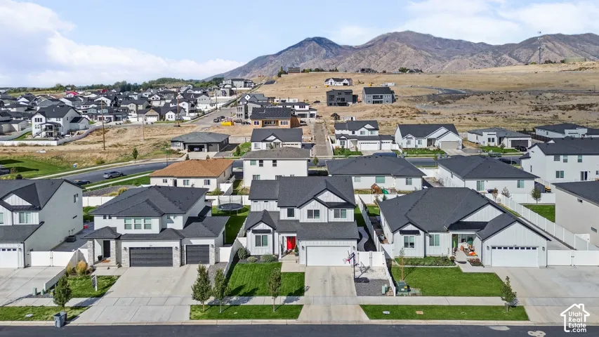 Aerial perspective of a multi-level suburban residence featuring a two-car garage, concrete driveway, front yard lawn, and mountain backdrop