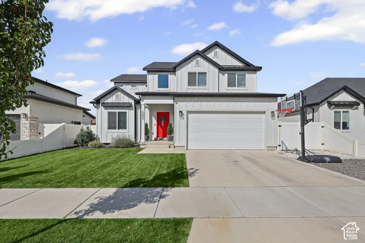 Two-story residence featuring white board-and-batten siding, a dark metal-accented roofline, an attached two-car garage, and a manicured front lawn