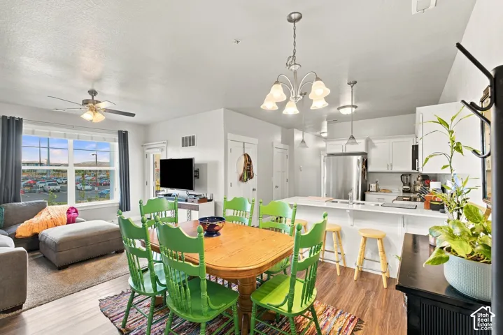 Open-concept living space featuring a wood-finish dining table with coordinating seating, abundant natural light from expansive windows, pendant and chandelier lighting fixtures, white cabinetry with stainless steel appliances, wood-finish flooring throug