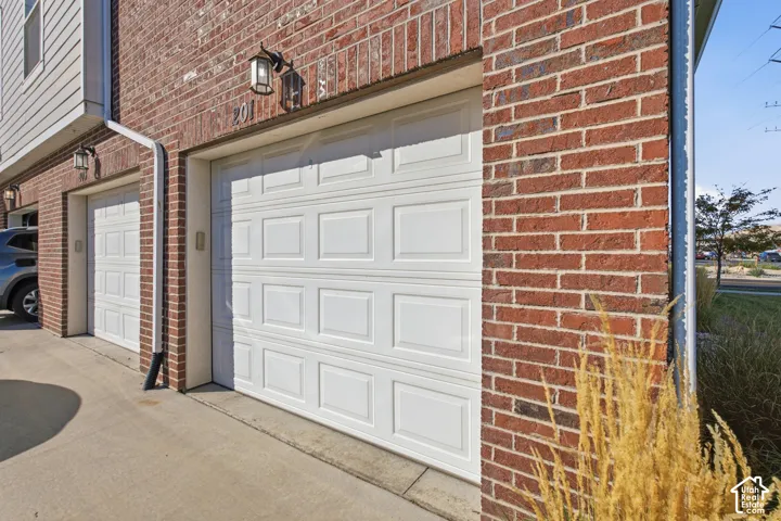 Brick exterior featuring two white garage doors with panel detailing, exterior sconce lighting, and a downspout system