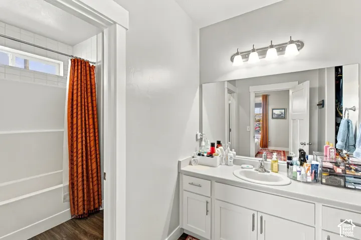Bathroom featuring a single vanity, a large wall-mounted mirror, brushed nickel light fixture, a shower-tub combination, and wood-finish flooring