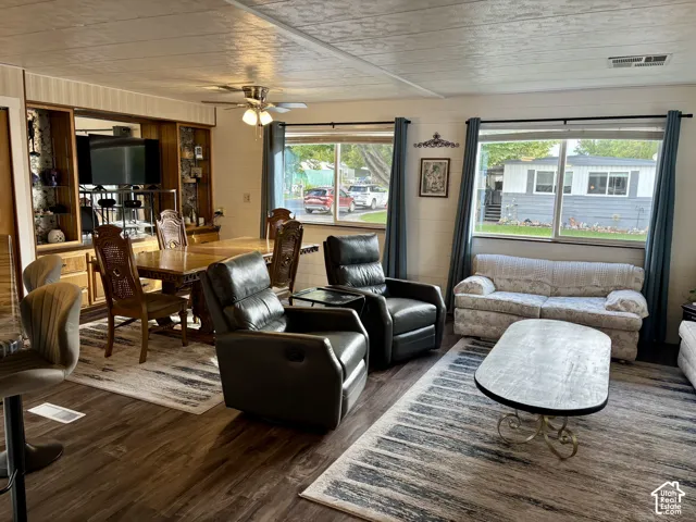 Open-concept living space featuring wood-finish flooring, built-in wooden cabinetry, dual large windows, and a ceiling fan