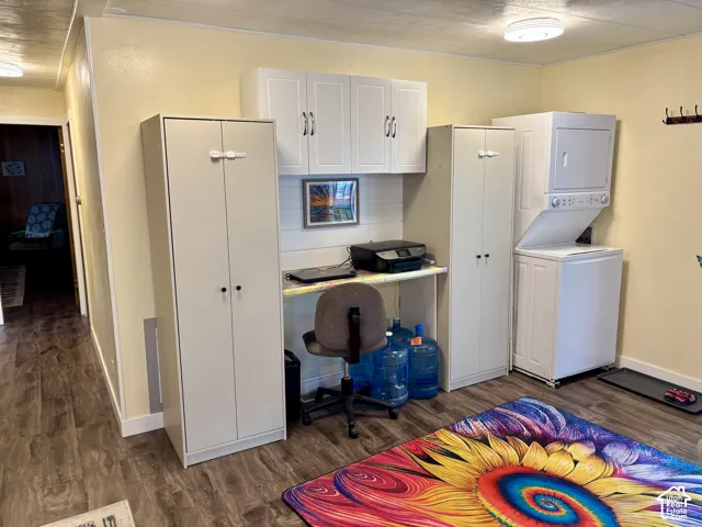 Built-in white cabinetry, integrated desk workspace, white overhead storage units, wood-finish flooring, and stacked laundry unit