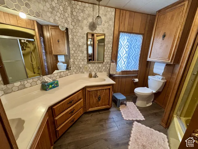 Bathroom featuring a custom-shaped vanity with integrated sink, wood-paneled walls, hexagon tile backsplash, wood-finish flooring, and recessed cabinet storage