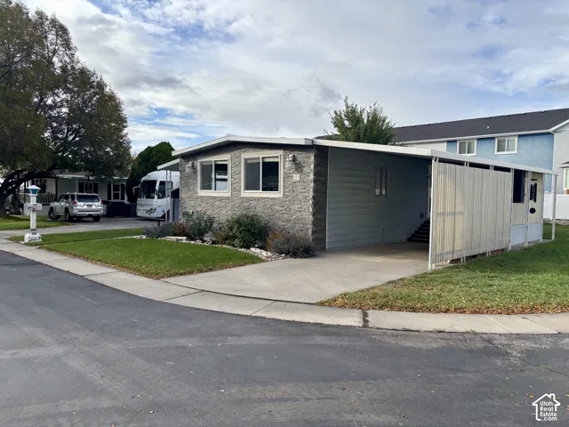 Exterior facade featuring stacked stone masonry, horizontal siding, attached carport with privacy screening, and concrete driveway