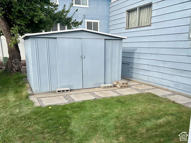 Metal storage structure featuring double doors situated on a stone paver and gravel ground cover