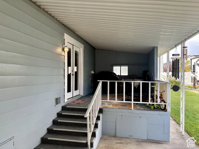 Covered exterior porch featuring light blue lap siding, white double doors with glass panels, a metal railing, and concrete steps