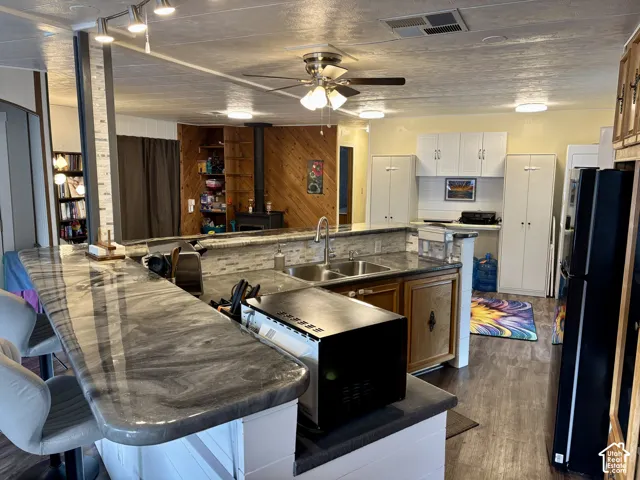 Kitchen featuring an expansive countertop with a marbled finish, dual-basin stainless steel sink, wood-finish flooring, white upper cabinetry, and a wood-paneled wall accent