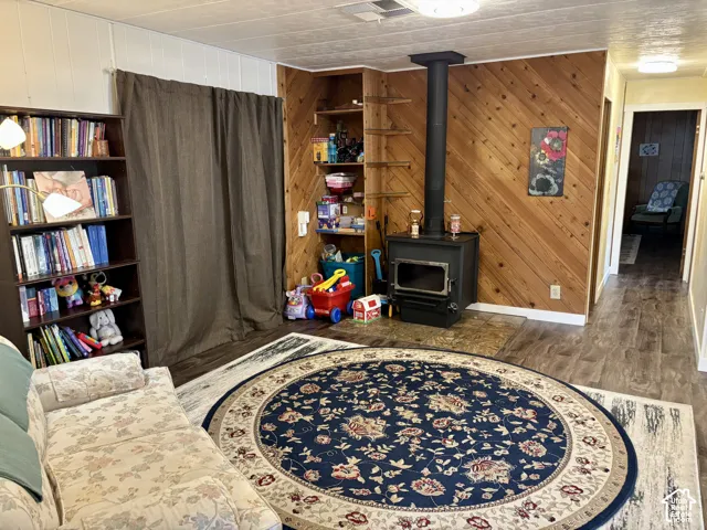 Living area featuring diagonal wood-panelled walls, a black metal wood-burning stove, built-in recessed shelving, and wood-finish flooring