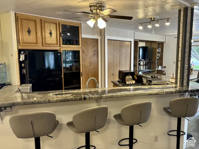 Kitchen featuring a stone-surface breakfast bar, wood cabinetry with glass-front display panels, a ceiling fan with integrated lighting, and multi-bulb track lighting