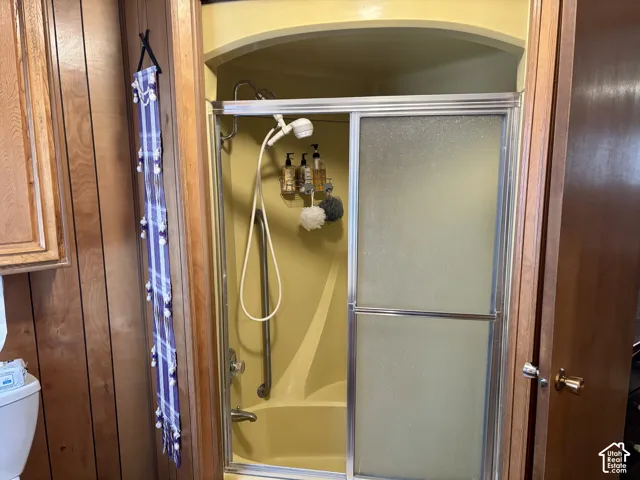 Walk-in shower enclosure with arched overhead molding, sliding glass doors, hand-held shower fixture, and a vertical metal grab bar