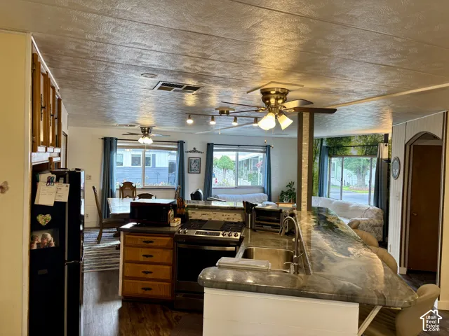Kitchen featuring a stone-surface breakfast bar, wood cabinetry, built-in stainless steel oven, range, and multiple overhead light fixtures