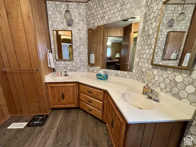 Dual-sink vanity with a solid-surface countertop, hexagonal tiled backsplash, wood paneling, wood-finish flooring, and wall-mounted mirrors
