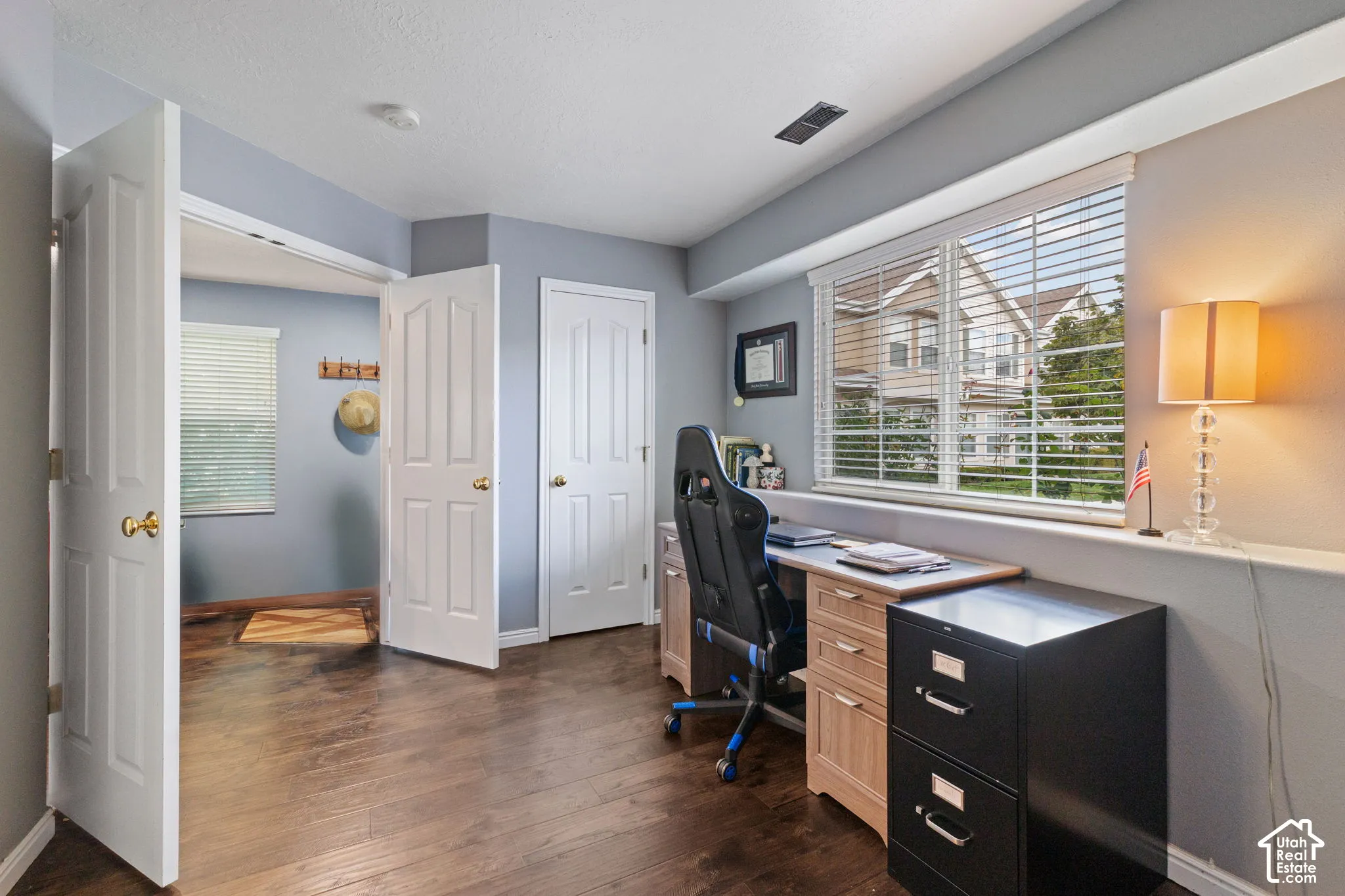 Room featuring wood-finish flooring, solid-core panel doors, and horizontal slat window blinds