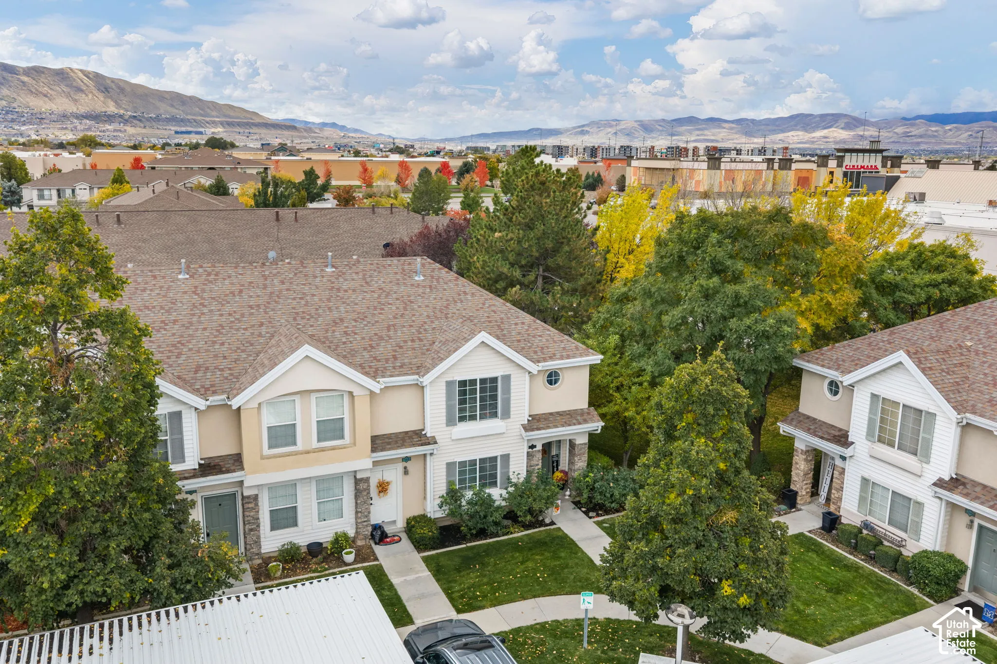 Two-story residential structure featuring a gable roof, tan stucco and stone veneer exterior, multi-pane windows with shutters, and surrounding landscaping