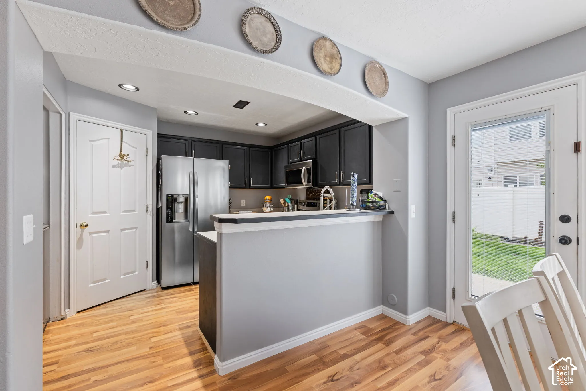 Kitchen featuring dark cabinetry, stainless steel appliances, breakfast bar with a solid surface countertop, recessed lighting, and wood-finish flooring