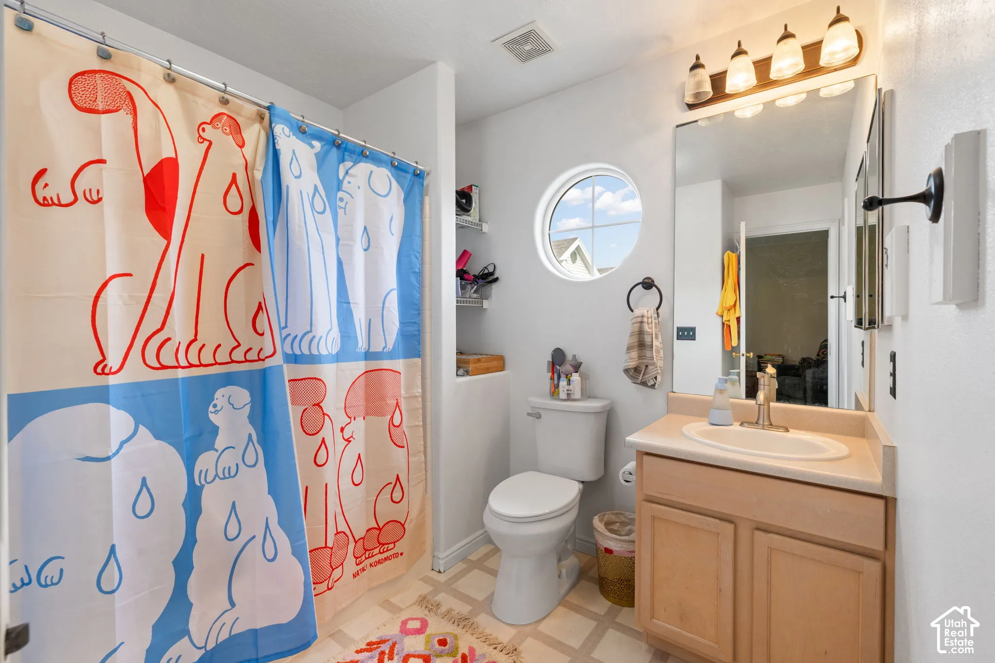 Bathroom featuring a single-sink vanity with a solid surface countertop, an oval wall mirror, circular window, and four-bulb vanity light fixture
