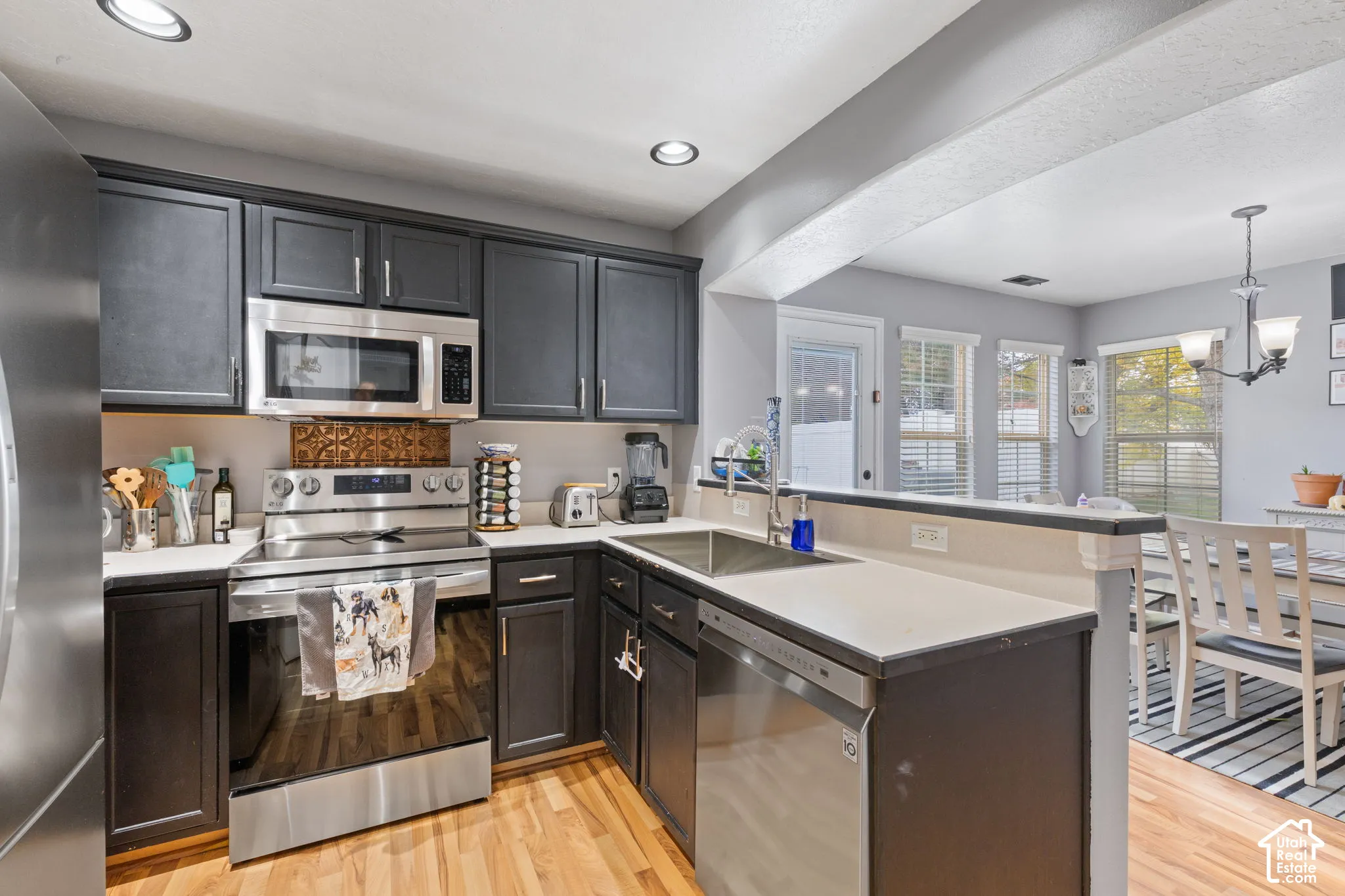 Kitchen featuring dark cabinetry, stainless steel appliances, neutral countertops, wood-finish flooring, and decorative metal backsplash tile
