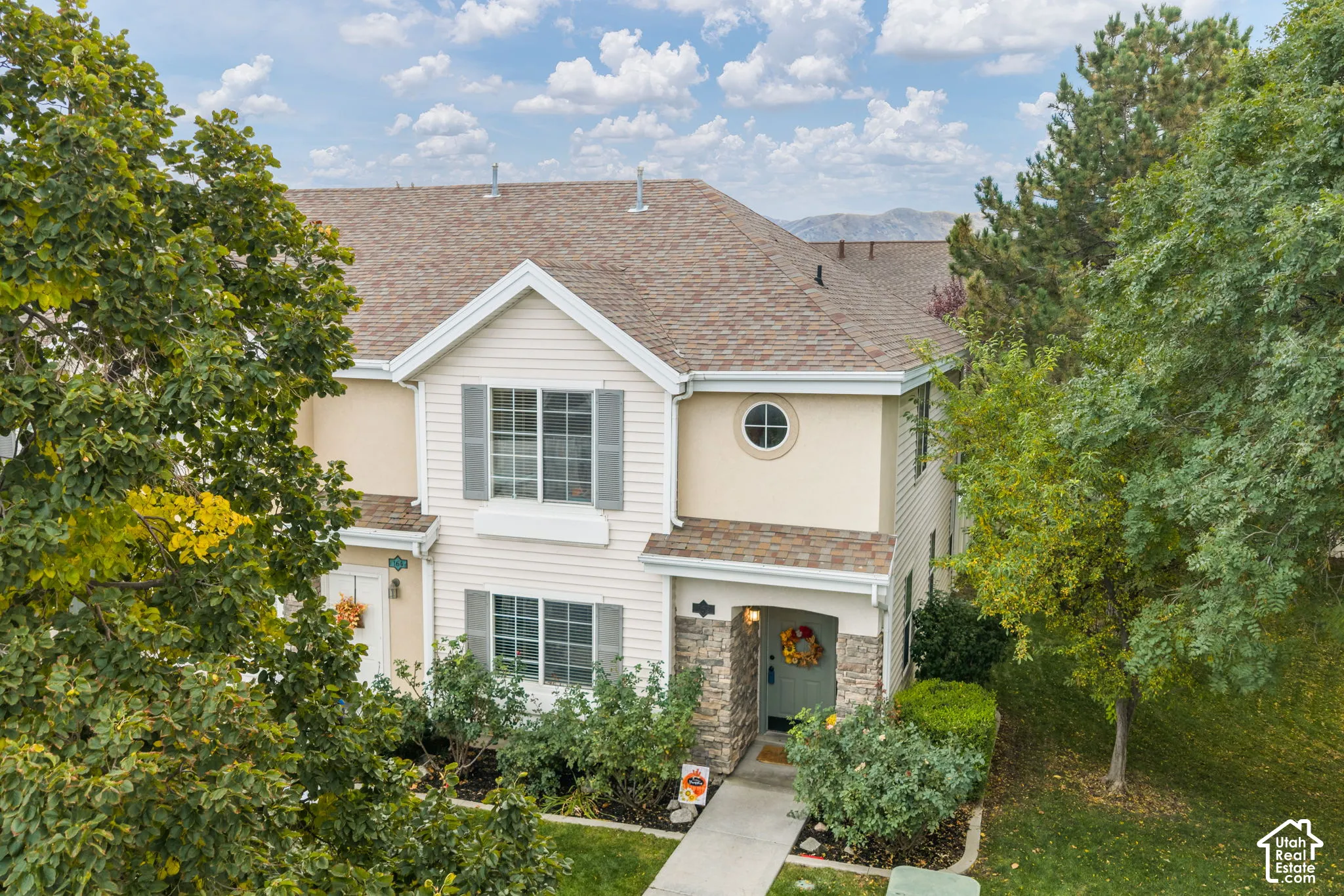 Two-story exterior featuring a mix of horizontal siding and stone veneer, shingle-style roof, decorative shutters, and a circular accent window