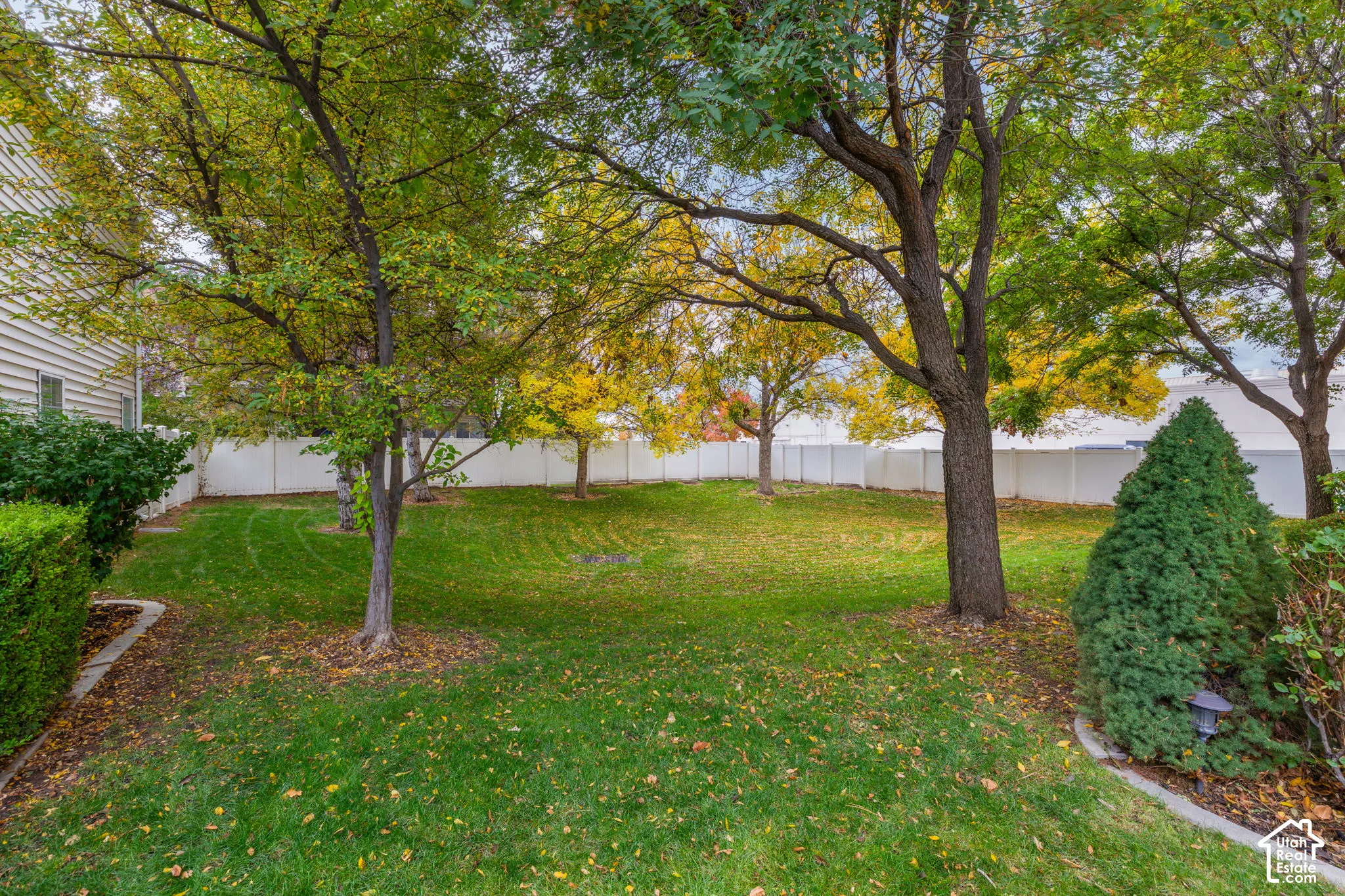 Backyard space featuring mature trees, manicured lawn, and white vinyl privacy fencing