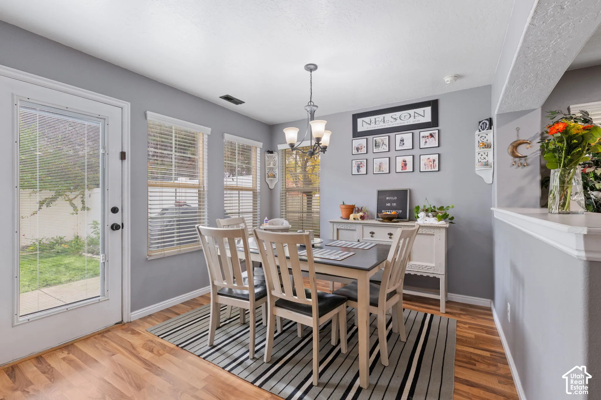 Dining space featuring wood-finish flooring, three vertical windows, a full-light glass exterior door, and a multi-arm overhead chandelier