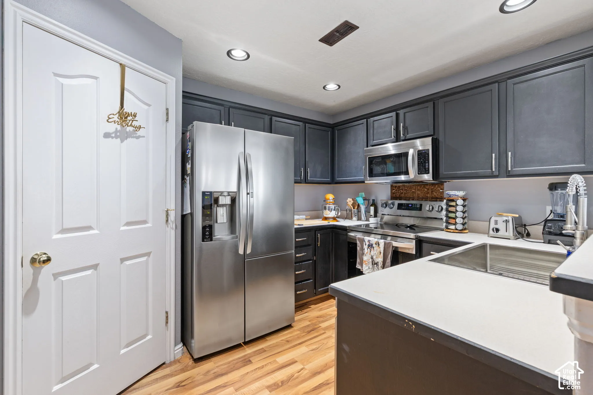 Kitchen featuring dark-toned cabinetry, stainless steel appliances, recessed ceiling lighting, light-toned countertops, and wood-finish flooring